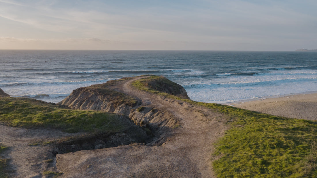 man runs on cliff path which ends at ocean and stops and looks out at ocean